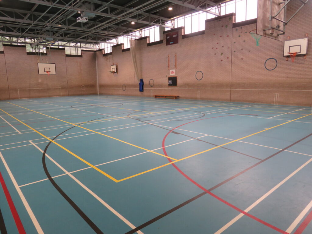 Archbishop Ilsley Catholic school and sixth form school's sports hall, with basketball hoops, football goals and courts/pitch.