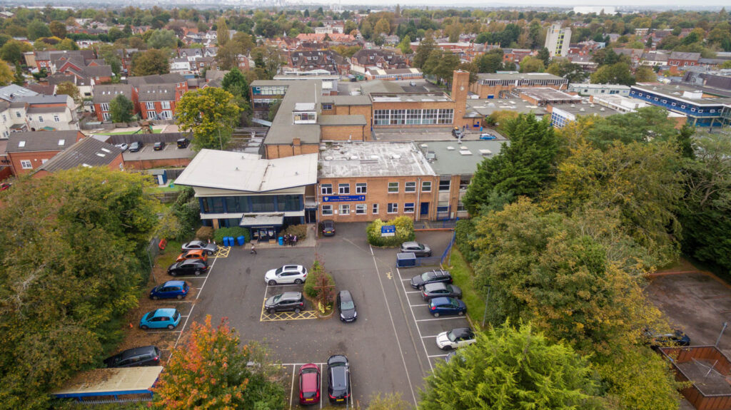 Outside arial shot, view of school. School building, carpark, trees and houses.