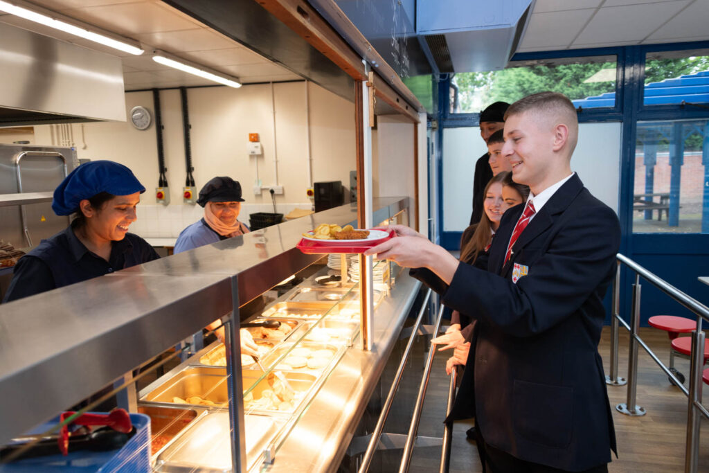 Pupils/student in the school canteen lining up for food lunch. Getting served by dinner staff.