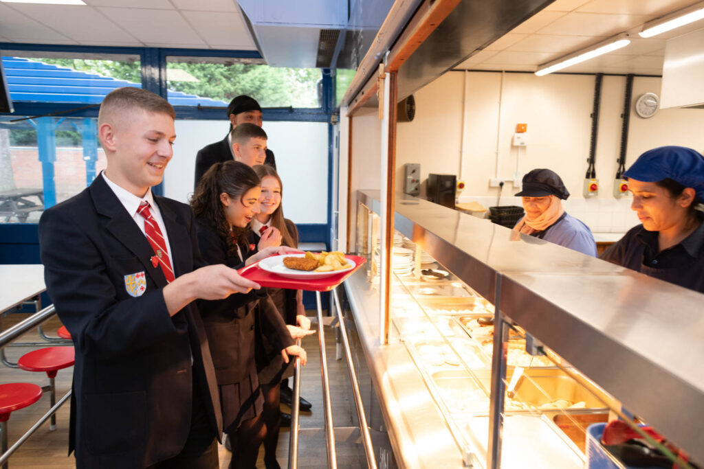 Pupils/student in the school canteen lining up for food lunch. Getting served by dinner staff.