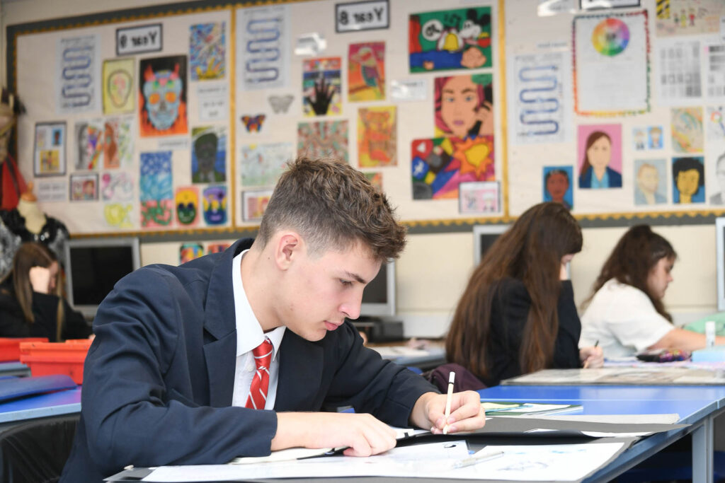 Class of pupils sitting down at desk's in classroom with open books. Pupil writing looking forward down at book.