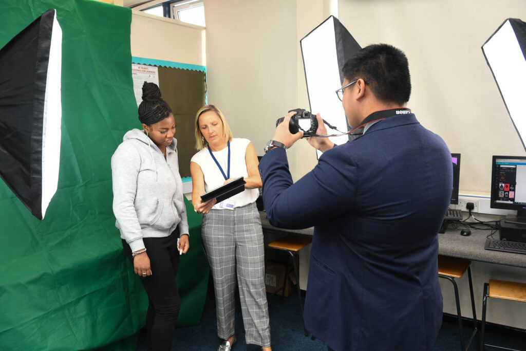 Pupil/student taking picture, of pupil and teacher in media space with studio lights and green screen drop back.