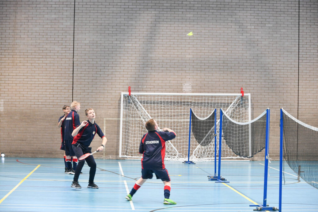 Pupils/students playing game of Badminton in class. In the indoor sports hall facility.