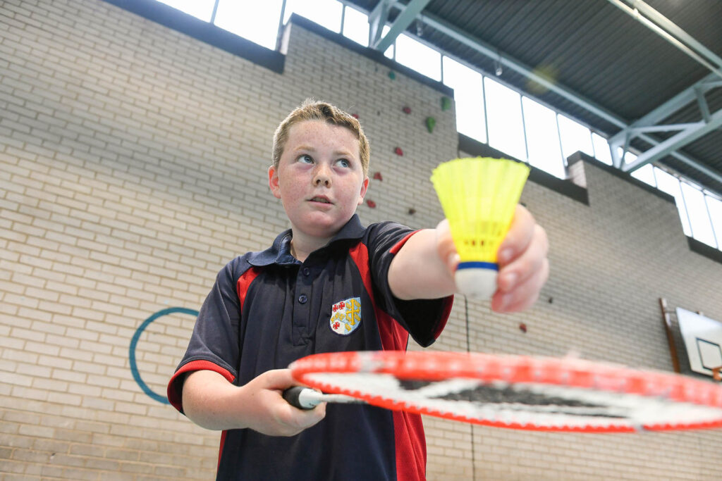 Pupil/Student in sports hall facility playing Badminton, ready to serve.
