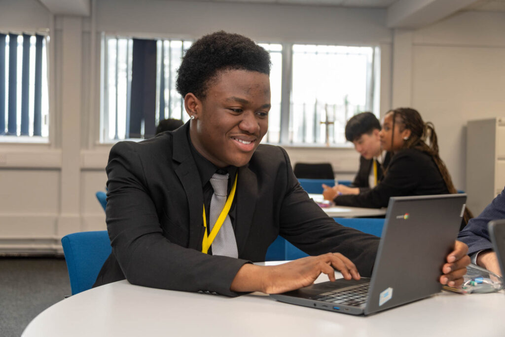 Six form pupils/students working at desks/tables, writing down work on laptop. In six form work space.