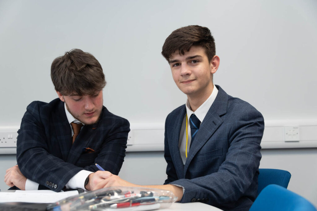 Six form pupils/students working at desks/tables, writing down work in books.