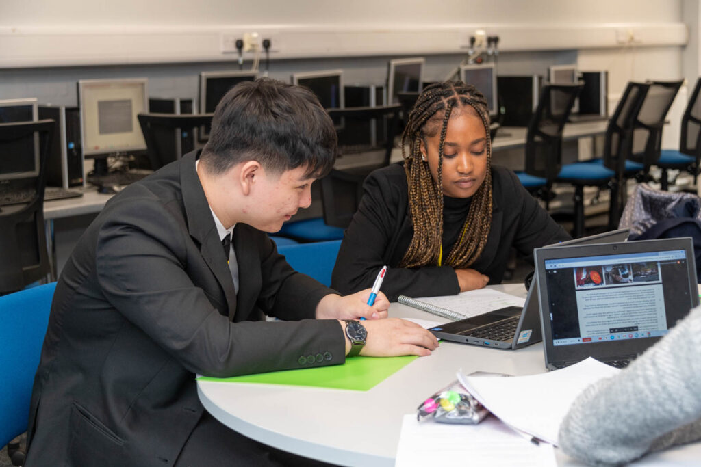 Six form pupils/students working at desks/tables, writing down work. In six form work space.