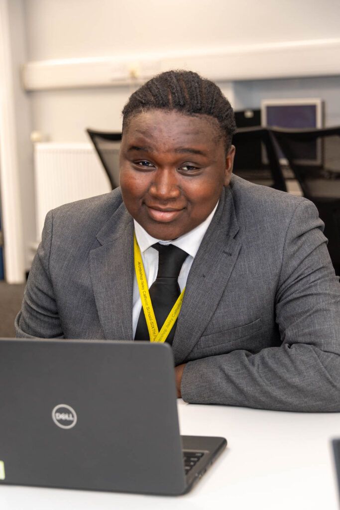 Six form pupil/student working at desk/table, writing down work. on laptop.