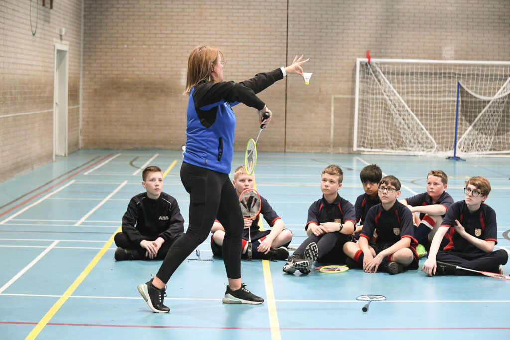 Pupils/students in sports hall with teacher getting lesson demonstration on Badminton.
