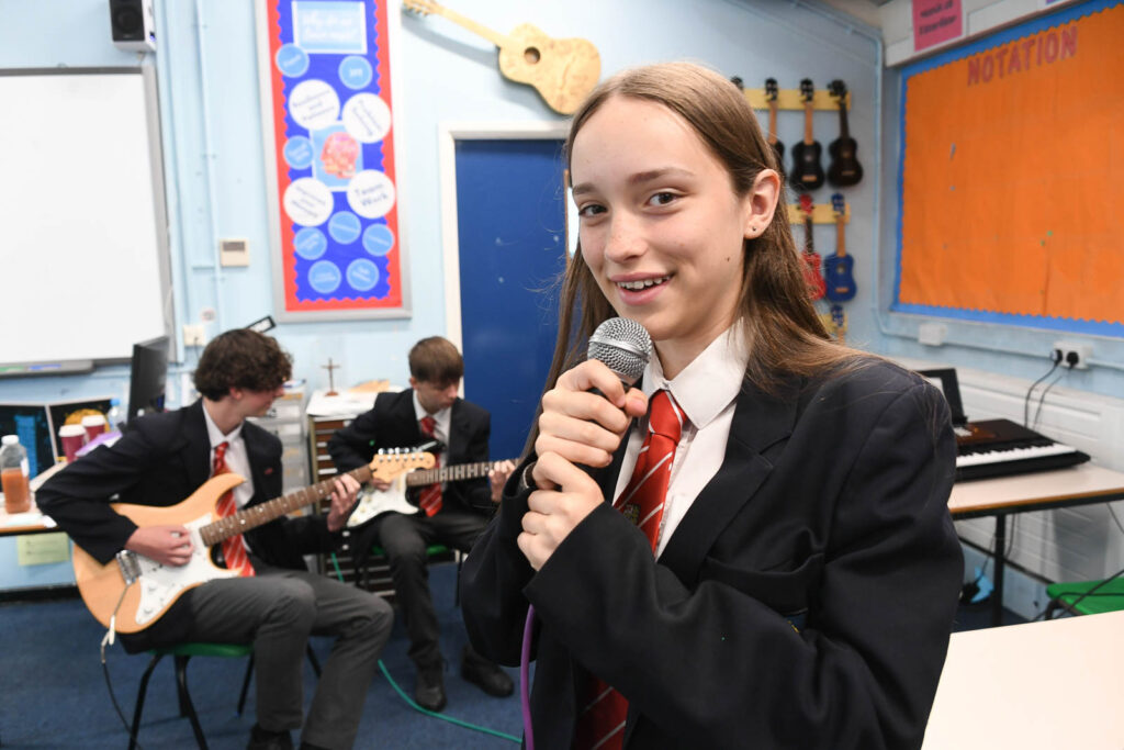 Music class room pupils having band practice jam. Pupil holding microphone ready to sing . The pupil in background playing on guitar