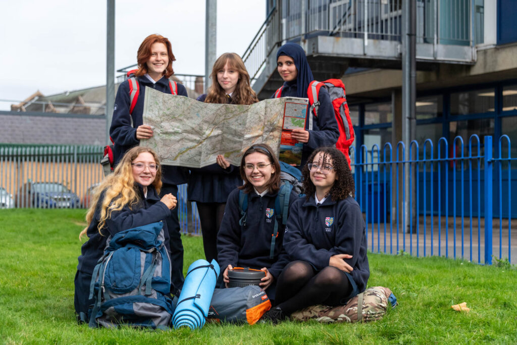 Pupils ready with camping gear, map out and backpacks on taking group photo on school grounds doing preparation.