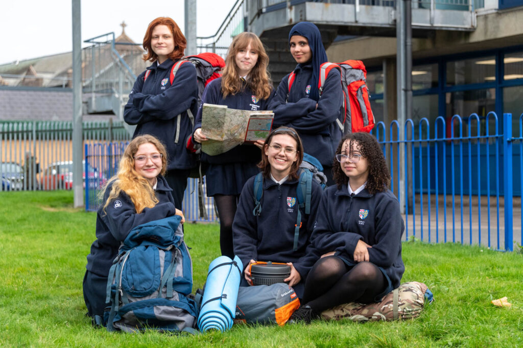 Pupils ready with camping gear, map out and backpacks on taking group photo on school grounds doing preparation.