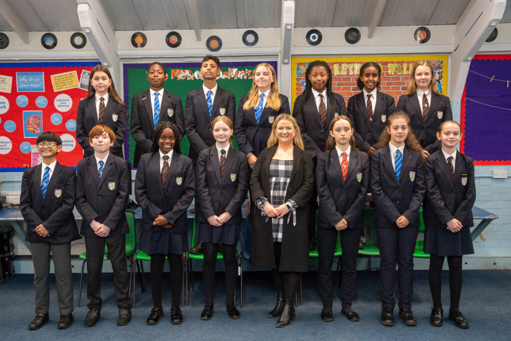 Whole class pupils and teacher standing posturing forward. Students at back standing on chairs. Vinyl records on the walls and informational posters and paper decors.