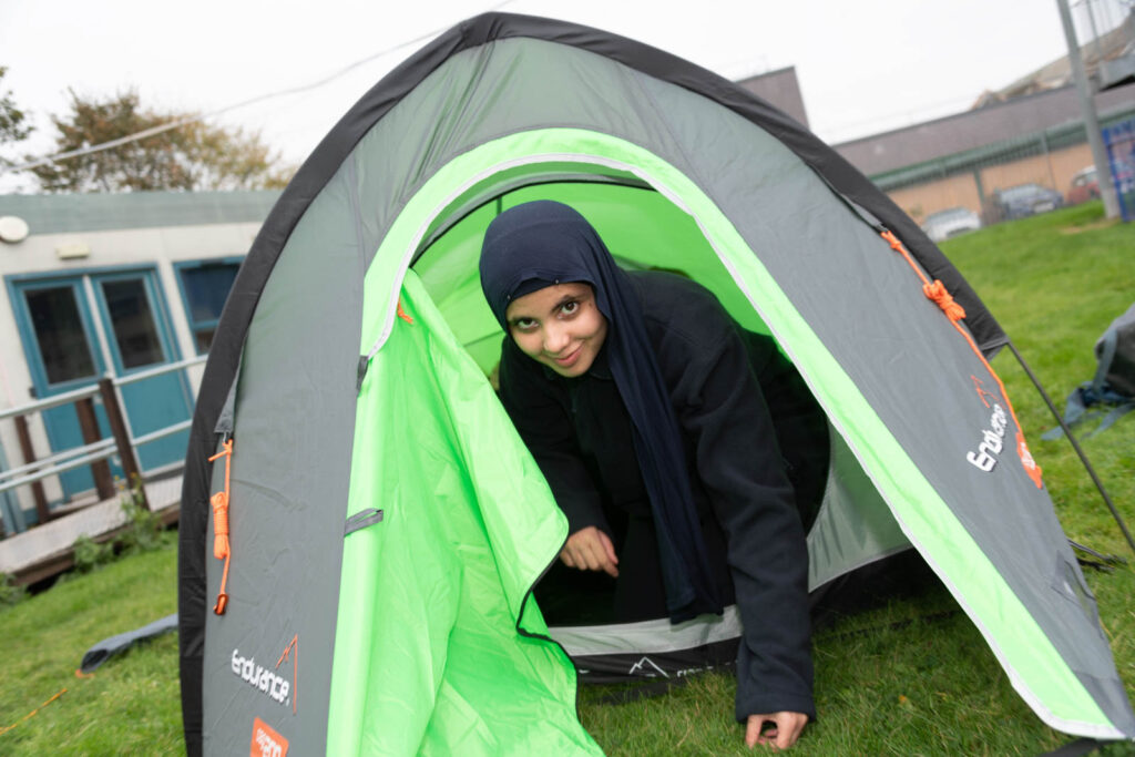 Pupil looking forward and coming out of set up tent on school grass ground premises.