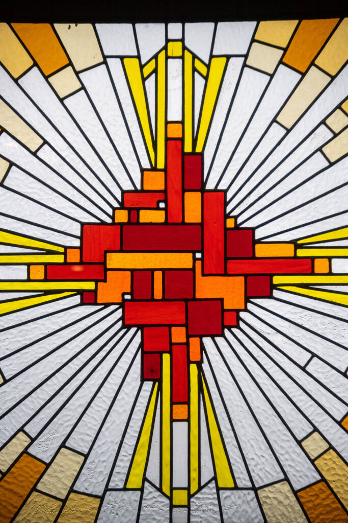 Stained glass window of abstract cross design, colours red, orange and yellow.