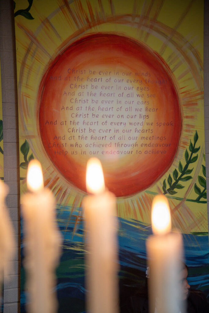 Christian Poster with text about Christ and sun over water on wall. In front a pupil and lit candles.