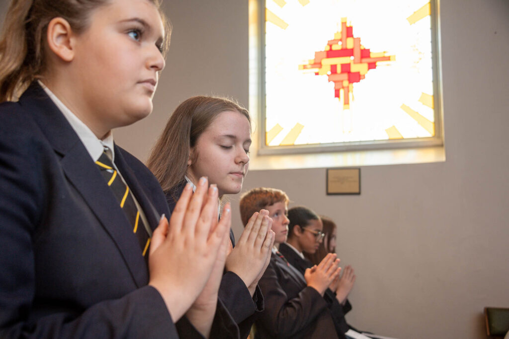 Pupils praying in Catholic mass. Stained glass window of abstract cross design .
