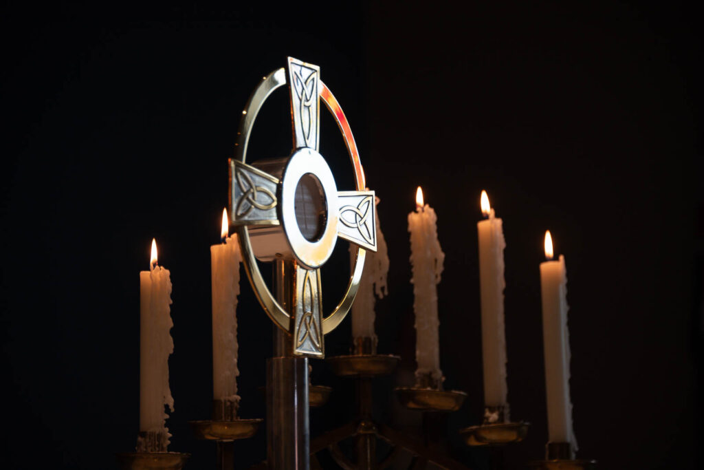 Cross statue icon with lit candles behind it with black background.