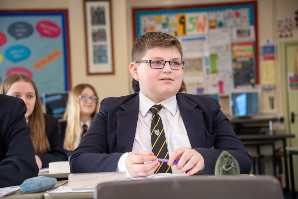 Class of pupils sitting down at desk's in classroom with open books looking forward to front of classroom.