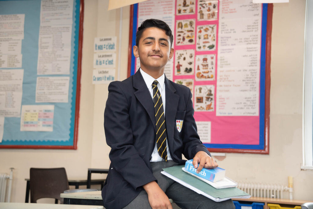 Pupil sat on desk in classroom looking directly ahead, with foreign language French books in hands.