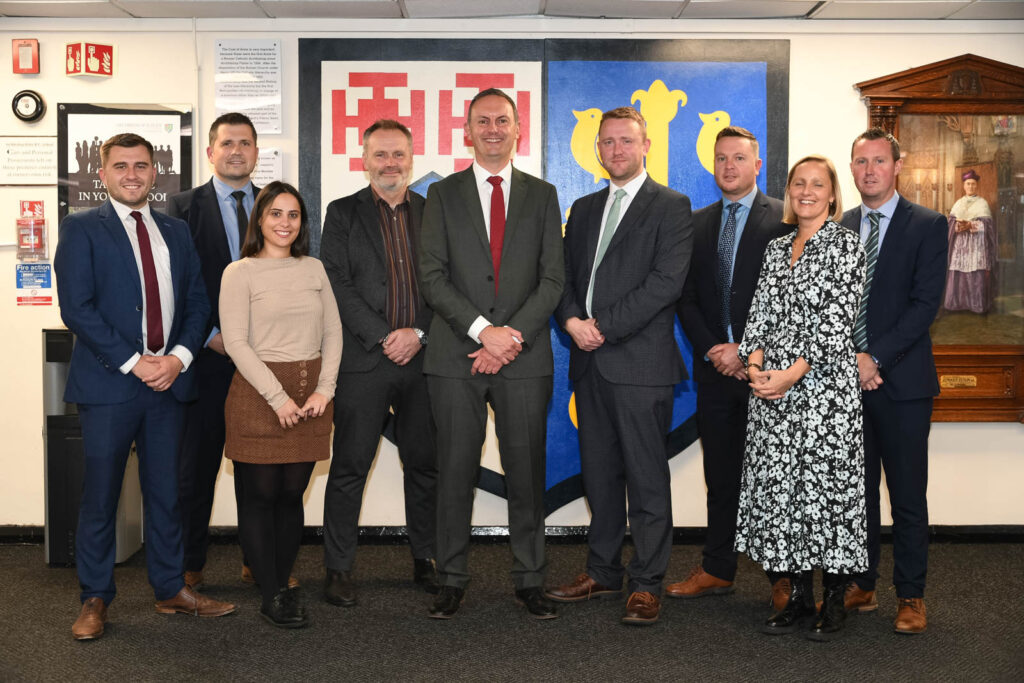 Staff member senior leadership group, in front of school logo emblem, in corridor . All looking directly ahead and posturing smart.