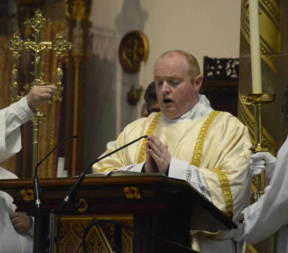 School chaplaincy priest doing a service in church. Deacon M.Casey at the altar praying surrounded by catholic religious icons.